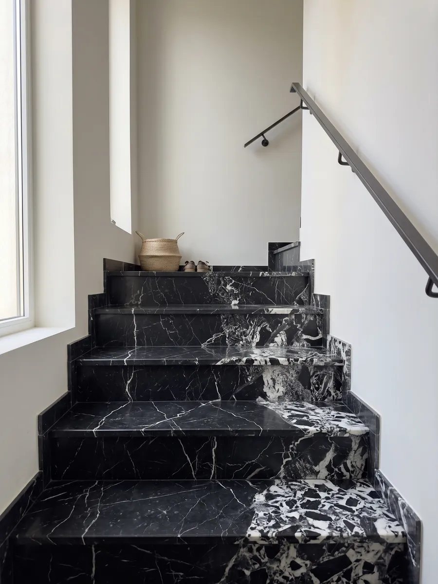 Interior staircase with black Grand Antique marble steps and a handrail: intense black with an area of broken white fragments that covers one side of the slab