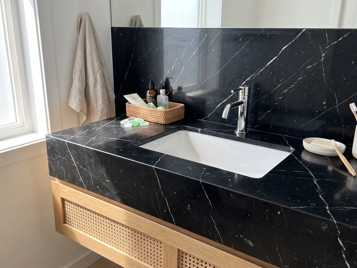 Vanity top and bathroom wall in black Nero Marquina marble with a white sink and chrome fittings: deep black with a few fine straight white veins