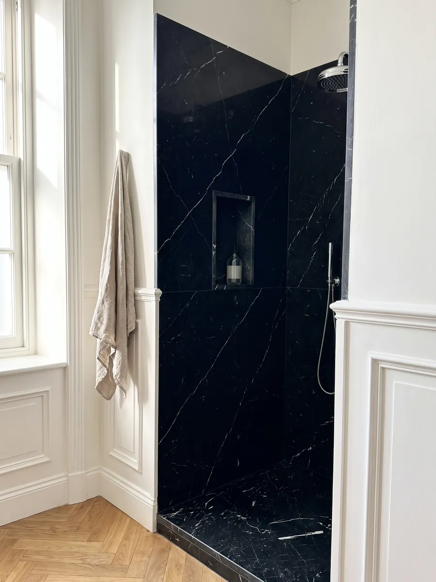 Shower clad in full black Nero Marquina marble slabs with a recessed niche: deep black with a few fine straight white veins