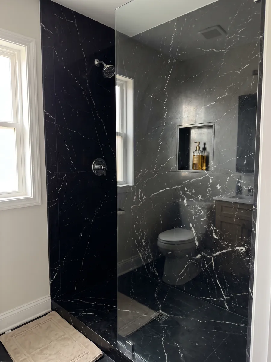 Shower clad in full slabs of Napoleon Black marble with a recessed niche: intense black with a crisp, irregular network of white veins