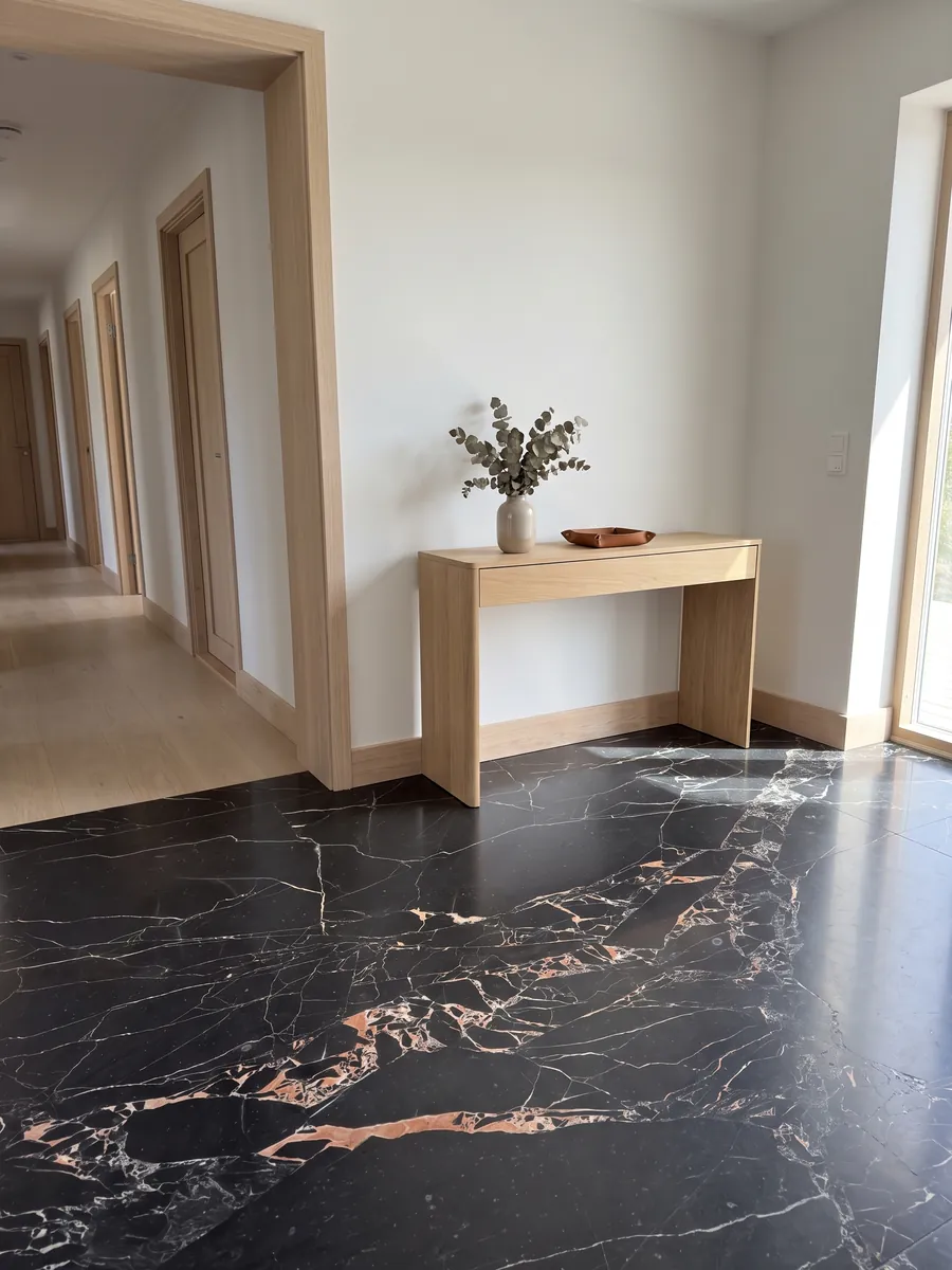 Entryway floor in large slabs of black Orange Black marble with natural light: black with fine white veins and clustered salmon-orange spots