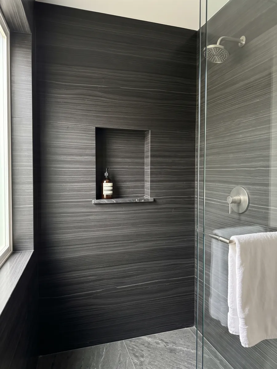 Shower clad in full Nero Pagoda marble slabs with a recessed niche: black with fine horizontal, parallel gray lines, almost like wood