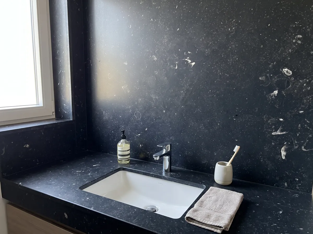 Vanity top and bathroom wall in black Pierre Bleu marble with a white sink and chrome fixtures: bluish black with small scattered light flecks