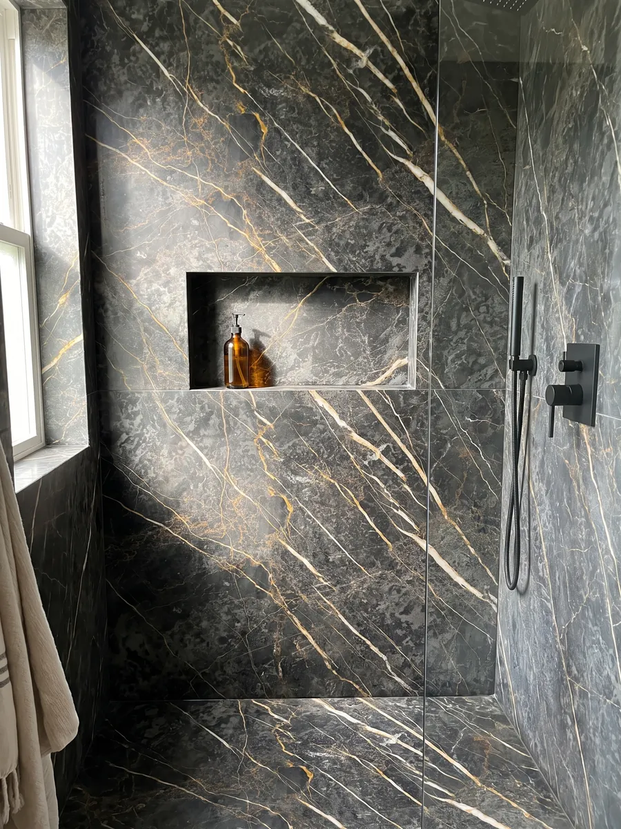 Shower clad in full black Port Laurent marble slabs with a recessed niche: charcoal gray with gold and white veins running parallel in a diagonal