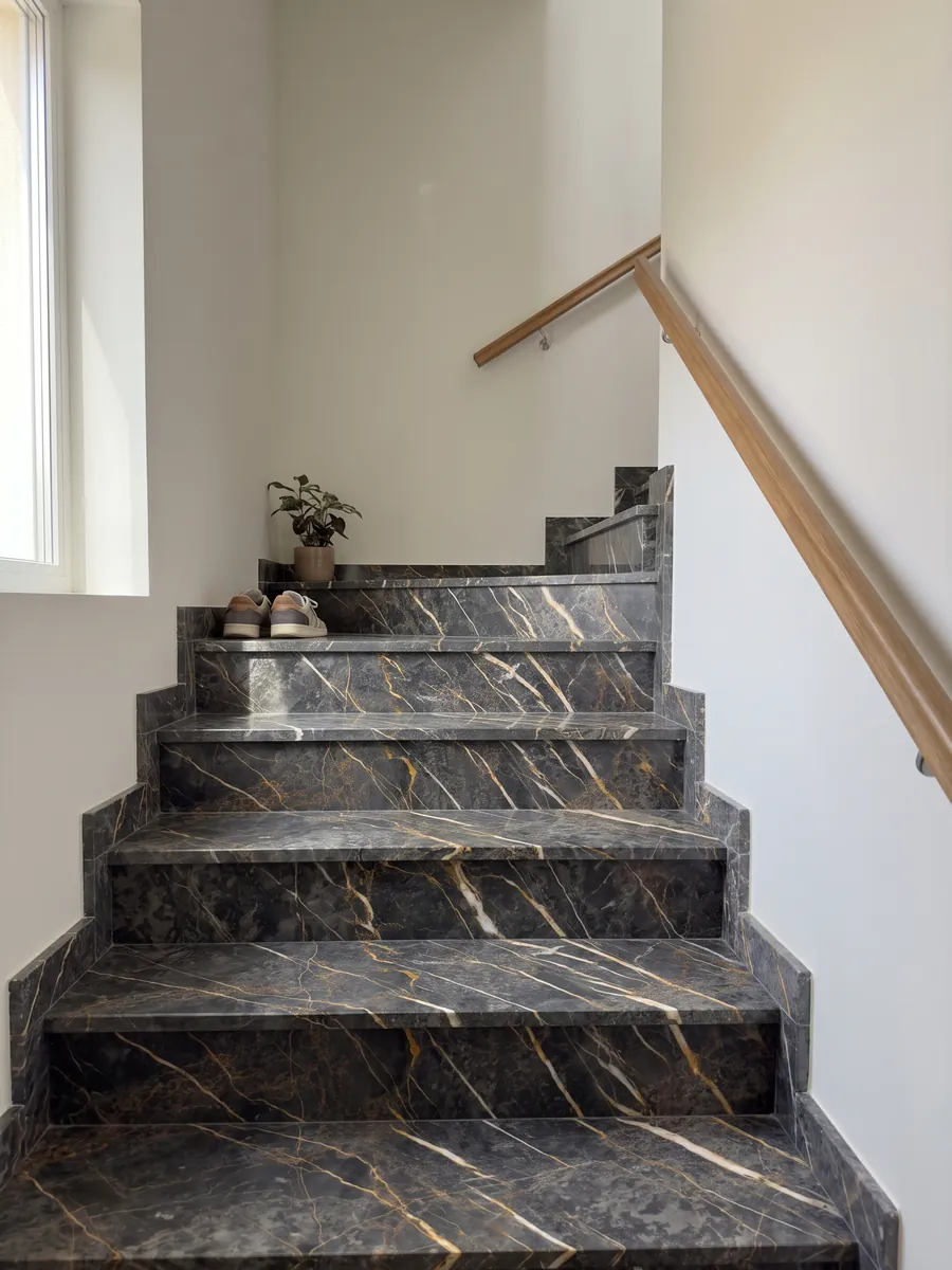 Interior staircase with black Port Laurent marble steps and a handrail: charcoal gray with gold and white veins running parallel in a diagonal
