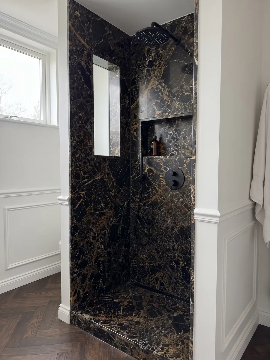 Shower clad in full slabs of black Portoro marble with a recessed niche: black fragments wrapped in a dense web of gold and white veins