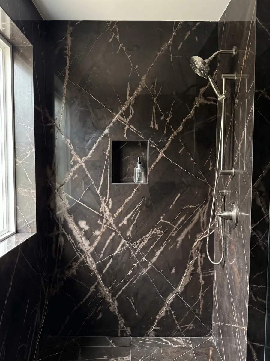 Shower clad in full slabs of black Sahara Bronze marble with a recessed niche: brownish black background with fine, crossing bronze-colored veins