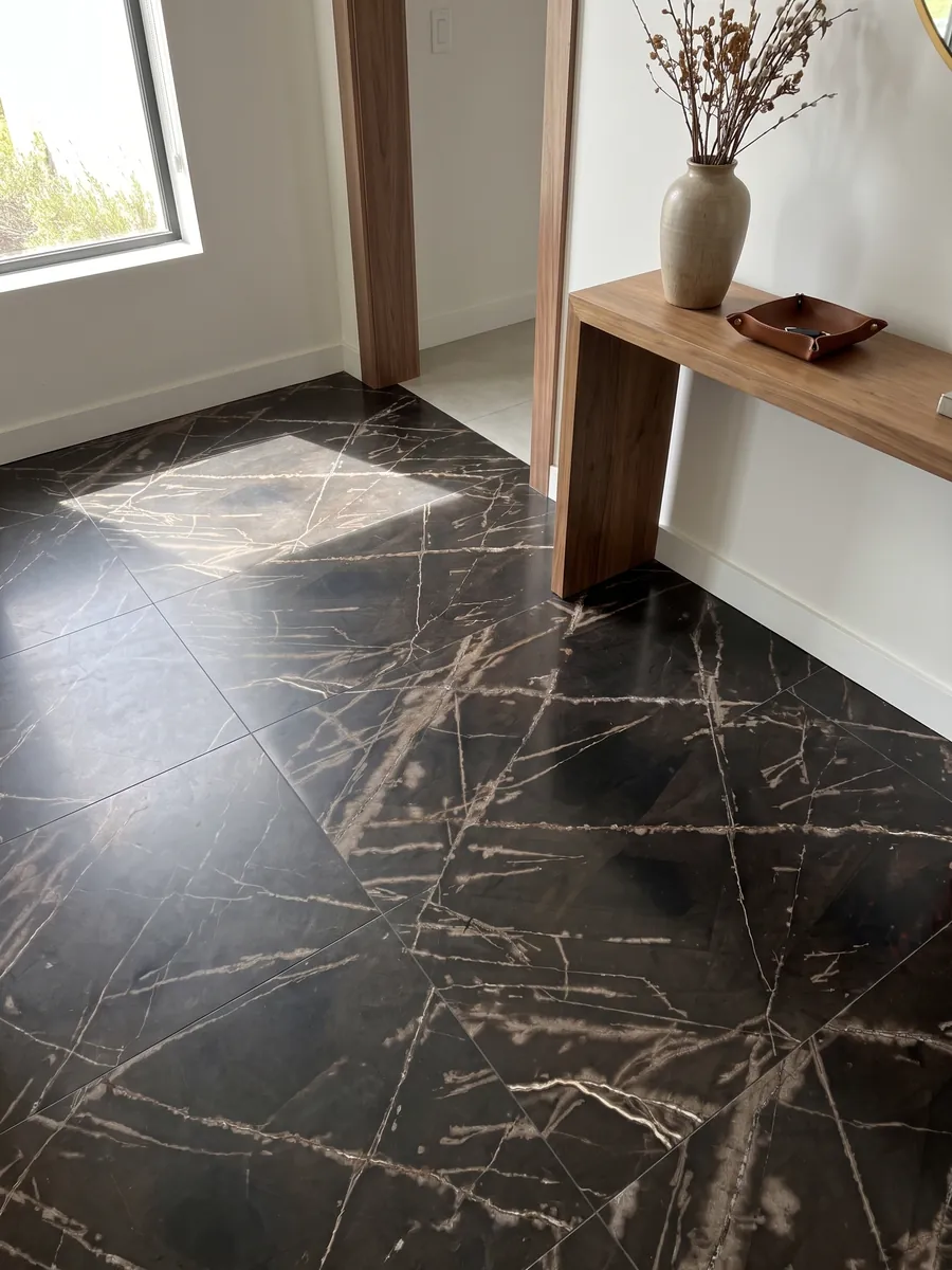 Entryway floor in large slabs of black Sahara Bronze marble with natural light: brownish black background with fine, crossing bronze-colored veins