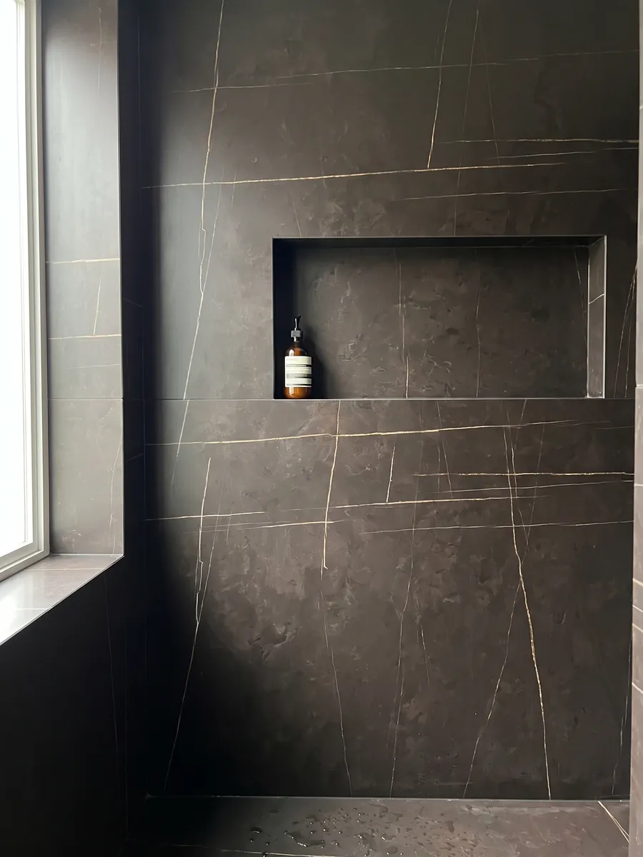 Shower clad in full slabs of Sahara Noir black marble with a recessed niche: brown-black with very fine, straight, sparse gold lines