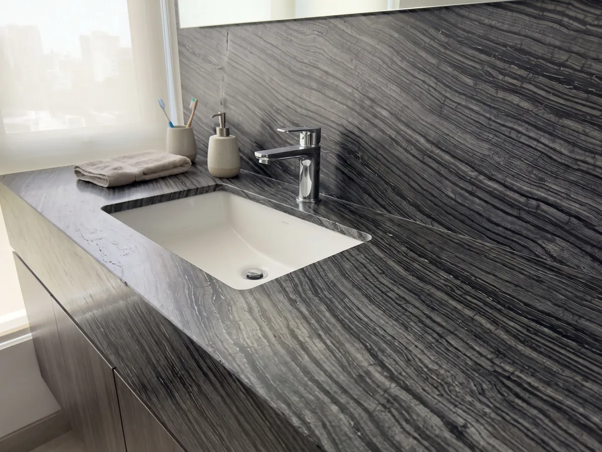 Vanity top and bathroom wall in black Zebrato marble with a white sink and chrome faucets: black with fine, wavy gray stripes running in diagonal, bark-like effect