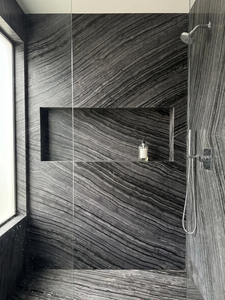 Shower clad in full slabs of black Zebrato marble with a recessed niche: black with fine, wavy gray stripes running in diagonal, bark-like effect