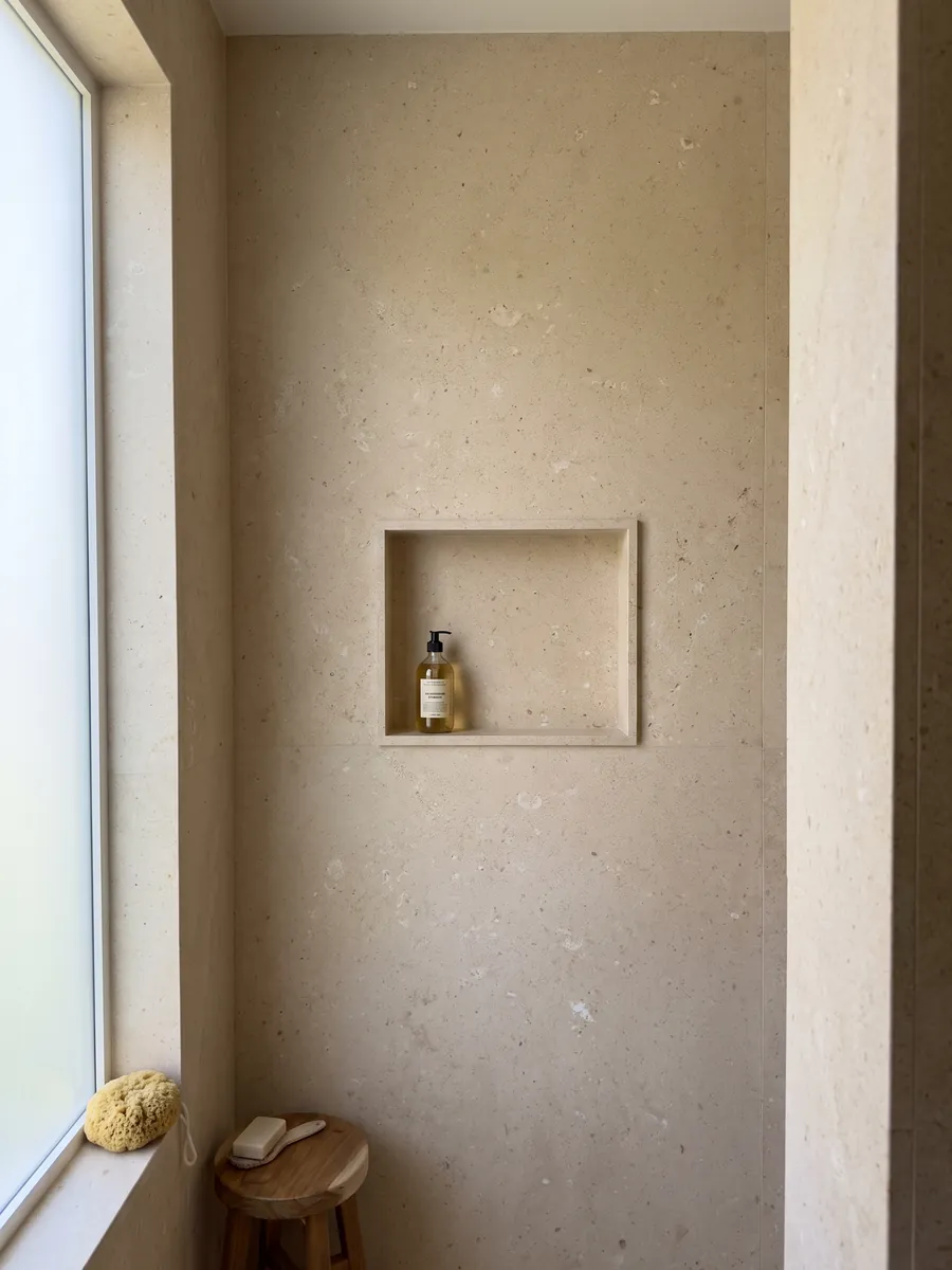 Shower clad in full Pietra di Vicenza Bianca marble slabs with a recessed niche: sandy beige with visible grain and small light fragments