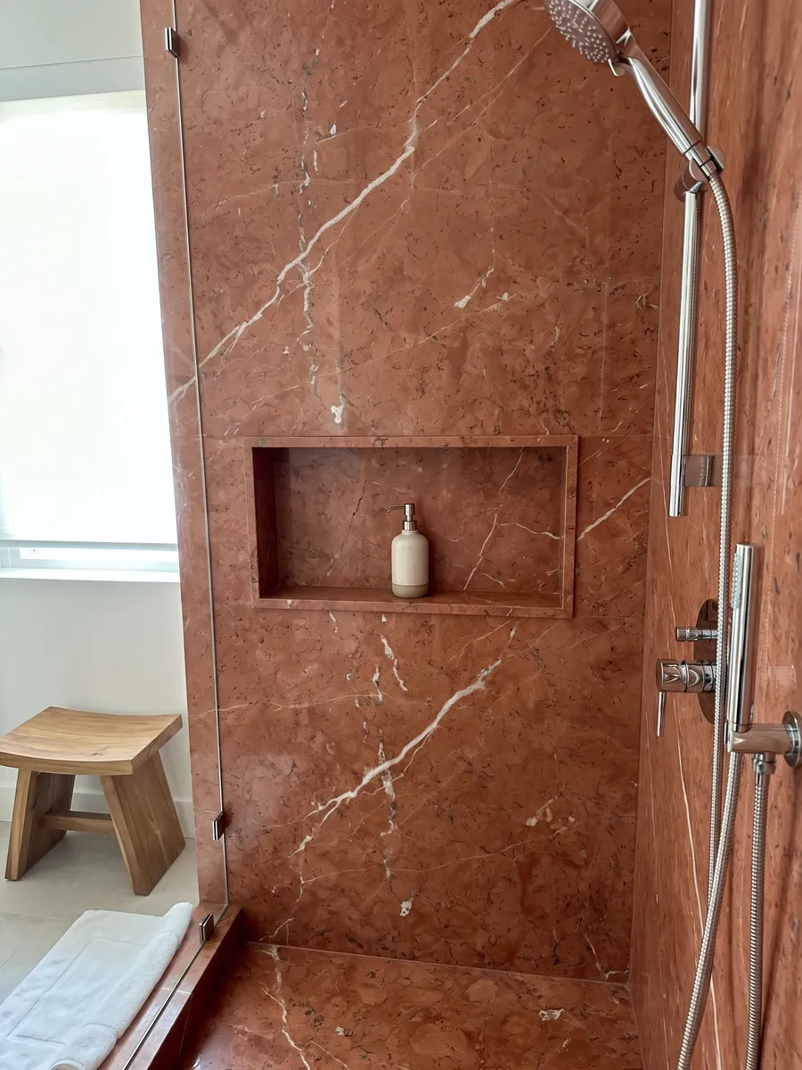 Shower clad in full Rojo Alicante marble slabs with a recessed niche: even terracotta red crossed by a few diagonal white veins