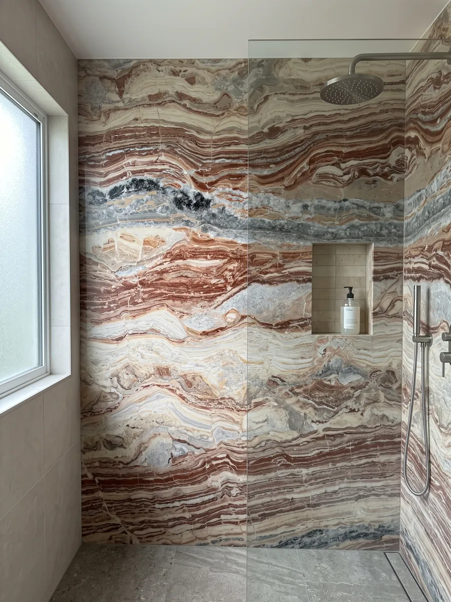 Shower clad in full slabs of red Arabescato Rosso marble with a recessed niche: wavy horizontal bands of brick red, cream and gray, with black spots at the top