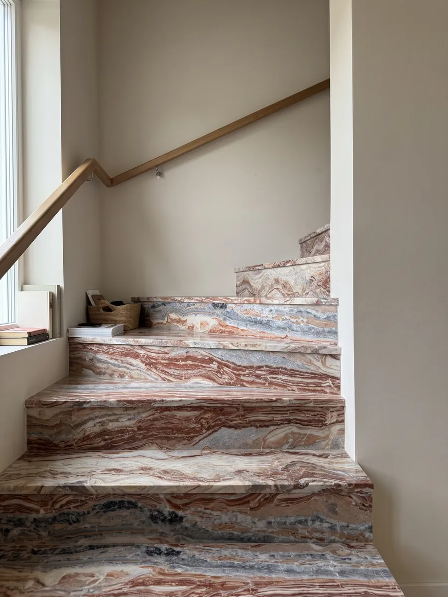 Interior staircase with red Arabescato Rosso marble steps and a handrail: wavy horizontal bands of brick red, cream and gray, with black spots at the top