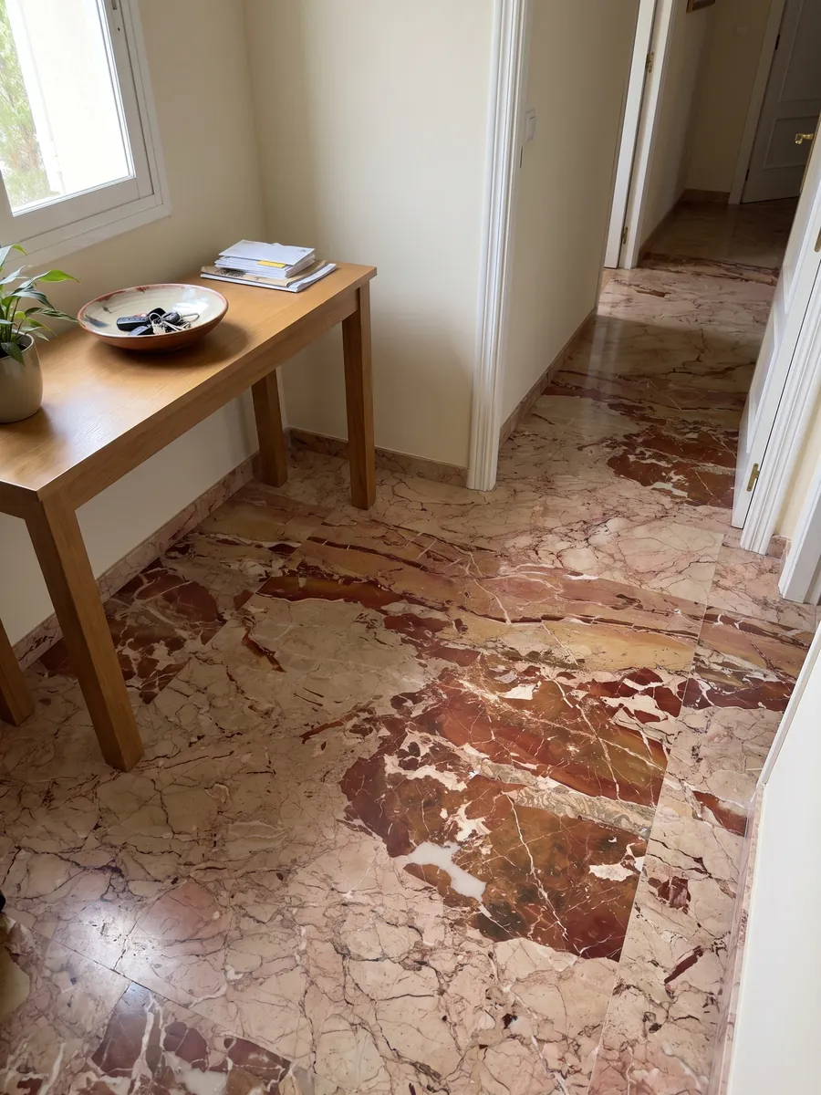 Entryway floor in large slabs of red Arlecchino marble with natural light: large rust-red patches on pinkish beige, crossed by fine white veins