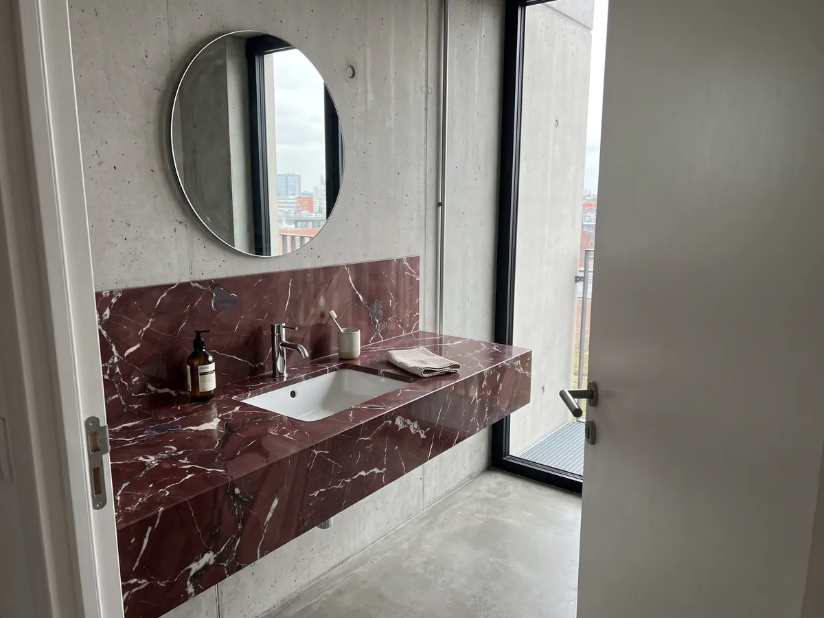 Vanity top and bathroom wall in Rosso Cardinale marble with a white sink and chrome faucets: burgundy red with irregular white veins and some gray-violet stains