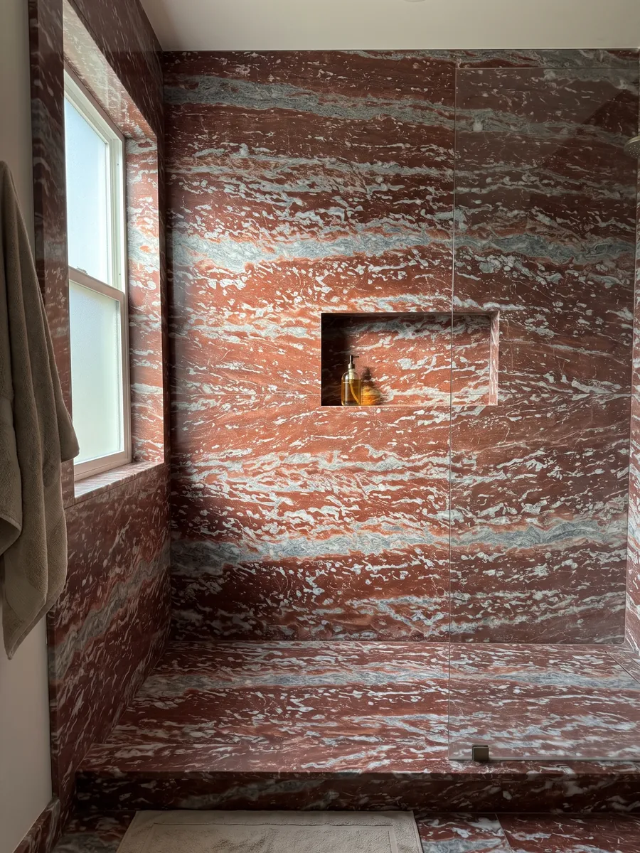 Shower clad in whole Rosso Francia marble slabs with a recessed niche: horizontal red stripes alternating with grayish-blue and white bands