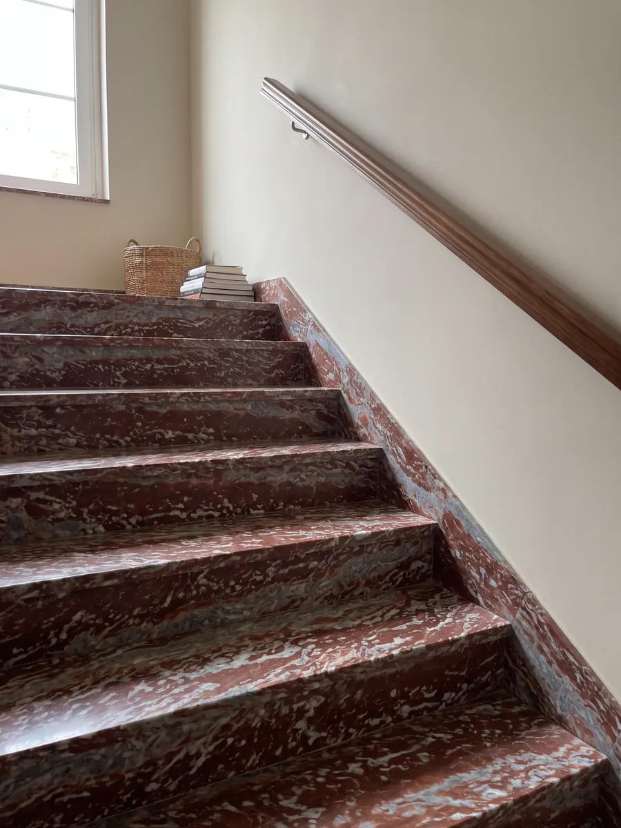 Interior staircase with Rosso Francia marble treads and a handrail: horizontal red stripes alternating with grayish-blue and white bands