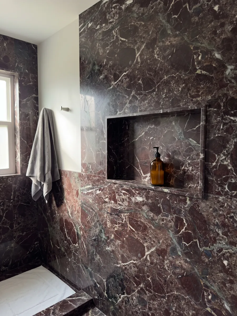 Shower clad in full slabs of red Rosso Levanto marble with a recessed niche: dark burgundy with gray-green areas and a network of white veins