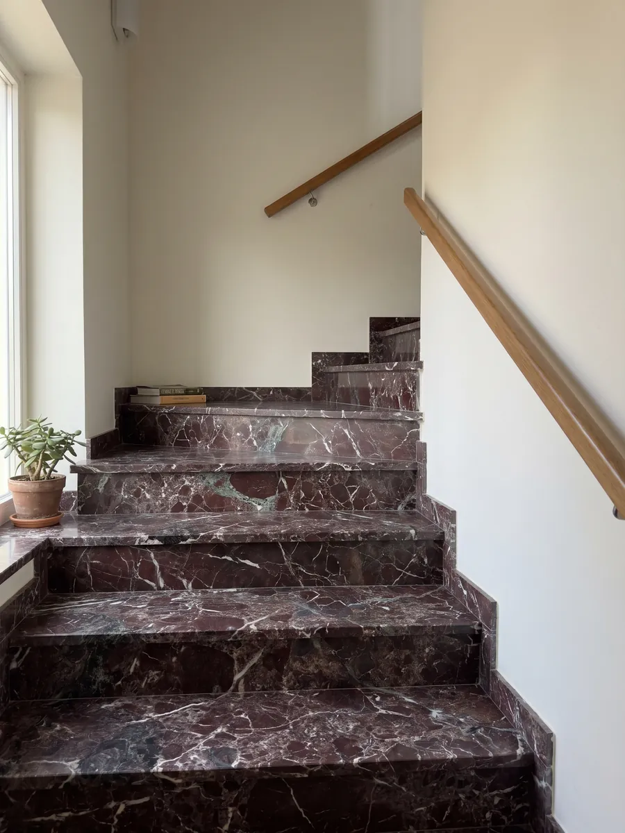 Interior staircase with red Rosso Levanto marble steps and a handrail: dark burgundy with gray-green areas and a network of white veins