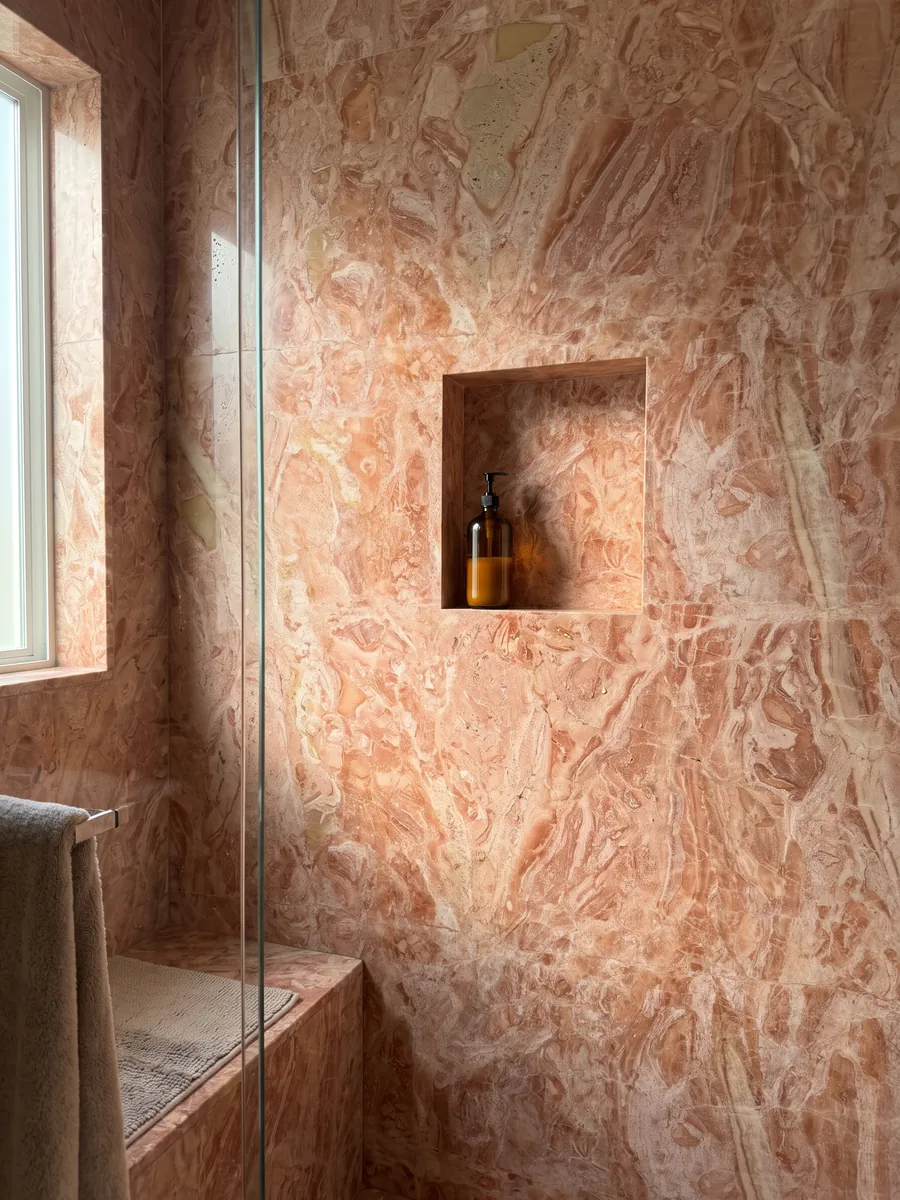Shower clad in full slabs of pink Breccia Bohemien marble with a recessed niche: a dense mix of coral and light beige fragments in salmon tones