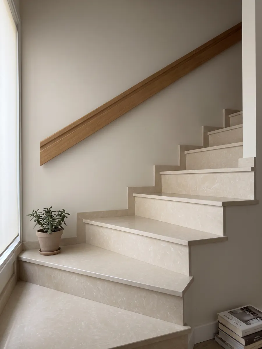 Interior staircase with Ecrù engineered marble with resin steps and a handrail: smooth, even cream surface with almost no pattern