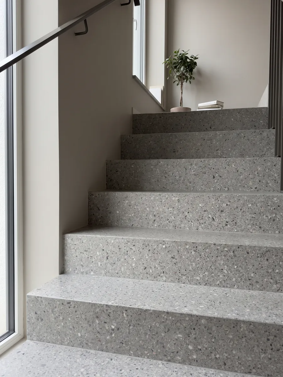 Interior staircase with Fior di Pesco Grey engineered marble with cement steps and a handrail: medium gray with small white and dark fragments, fine terrazzo style