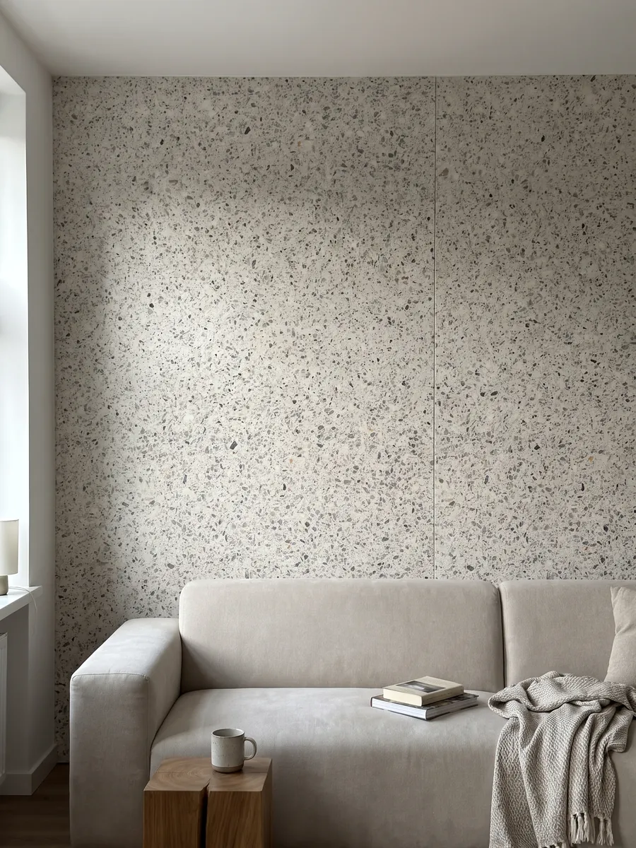 Living room wall clad in bookmatched slabs of Fior di Pesco White engineered marble with resin behind a sofa: ivory background with scattered gray and dark fragments, terrazzo style