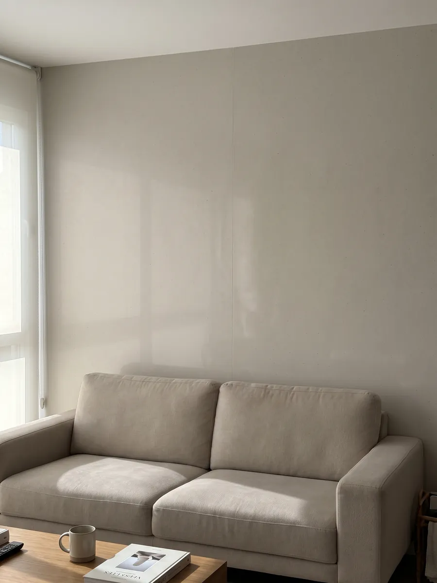 Living room wall clad in bookmatched slabs of Veselje engineered marble with resin behind a sofa: a flat warm pearl gray color; the image shows no texture, only a gradient of light