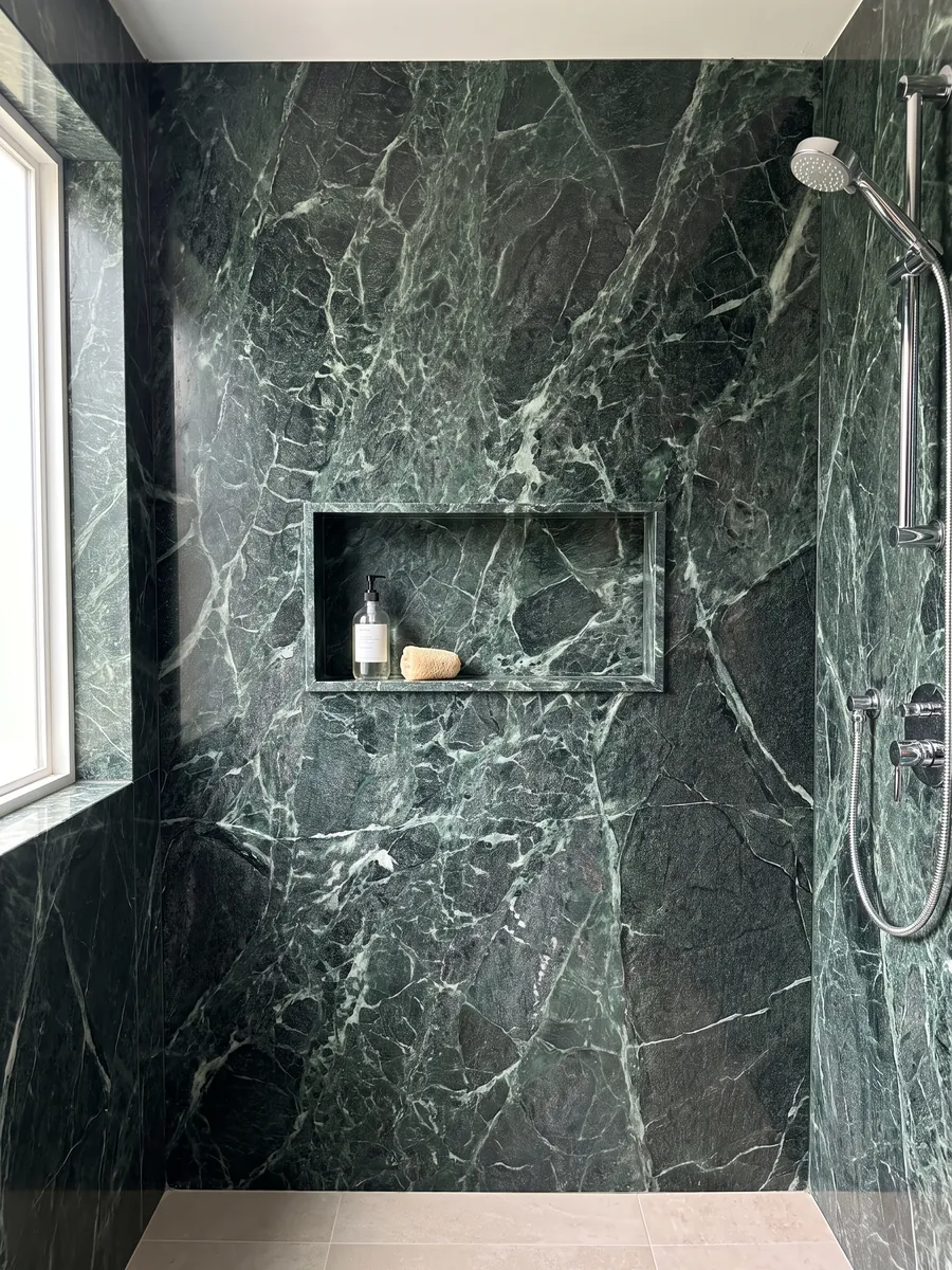 Ducha revestida com chapas inteiras de Mármore Verde Alpi com nicho embutido: verde quase preto atravessado por uma rede densa de veios verde-claro e brancos