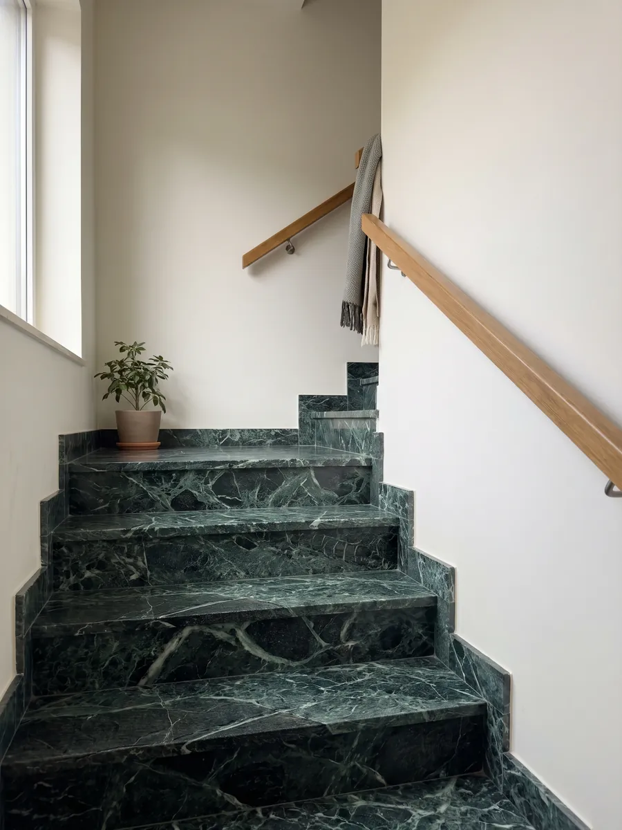 Escada interna com degraus de Mármore Verde Alpi com corrimão: verde quase preto atravessado por uma rede densa de veios verde-claro e brancos