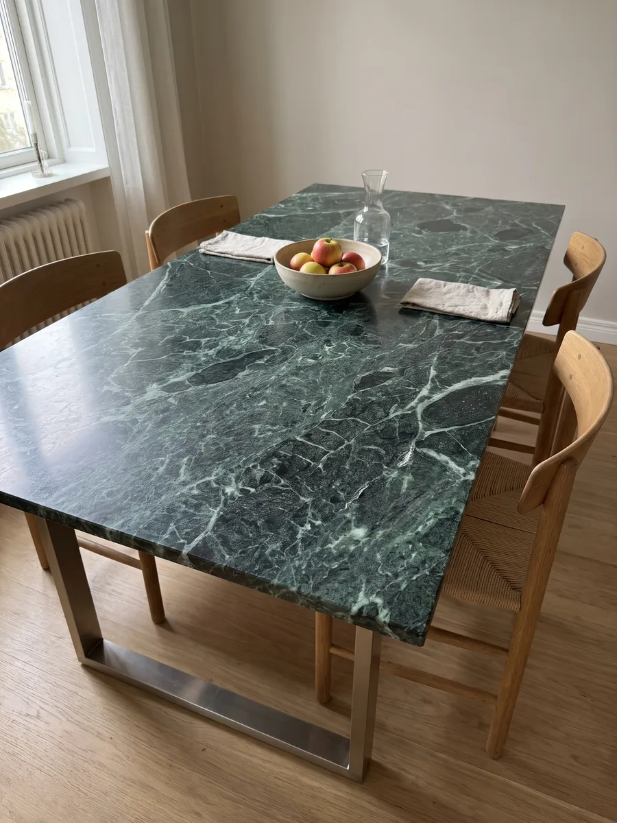 Mesa de jantar com tampo de Mármore Verde Alpi sobre base de aço: verde quase preto atravessado por uma rede densa de veios verde-claro e brancos