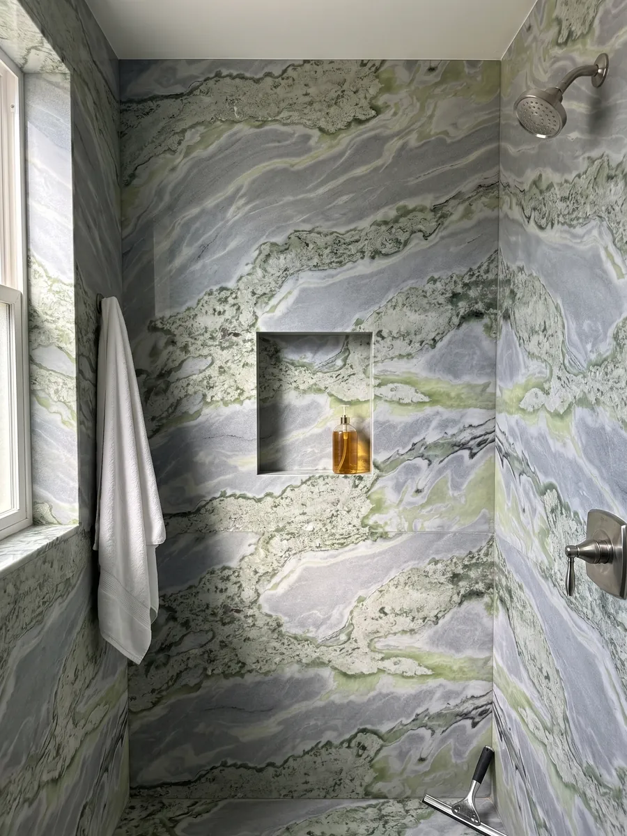 Shower clad in full slabs of green Bloody Mary marble with a recessed niche: waves of sage green and lime mixed with blue-gray; no red in the photo