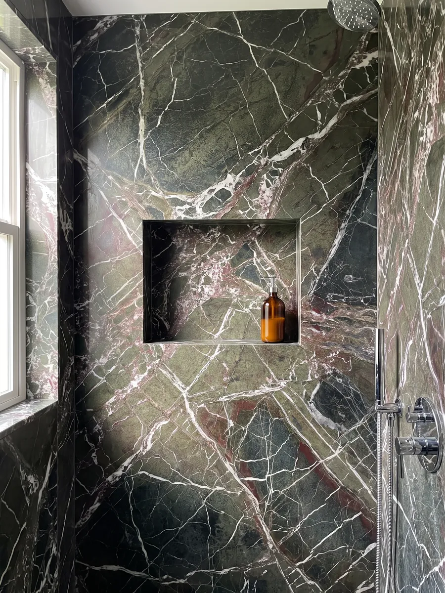 Shower clad in full Breccia Imperiale green marble slabs with a recessed niche: dark green with a web of straight white veins and small wine-red touches