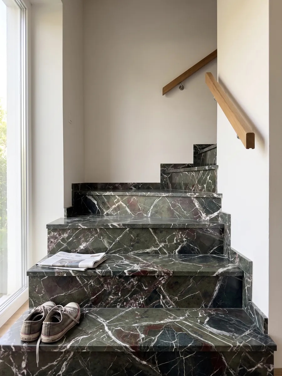 Indoor staircase with Breccia Imperiale green marble steps and a handrail: dark green with a web of straight white veins and small wine-red touches