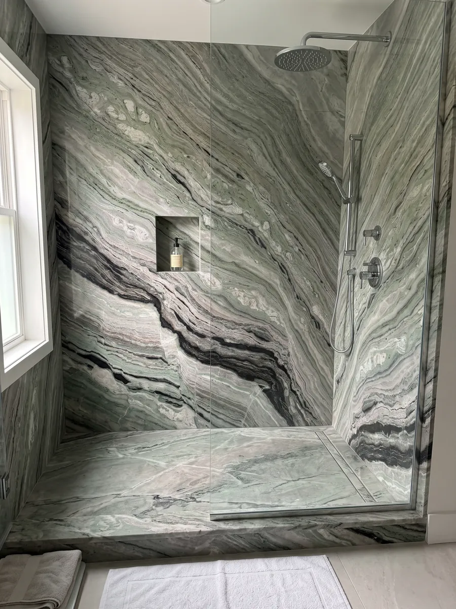 Shower clad in full slabs of green Camellia Green marble with a recessed niche: fine wavy greyish-green bands with a marked black band at the bottom