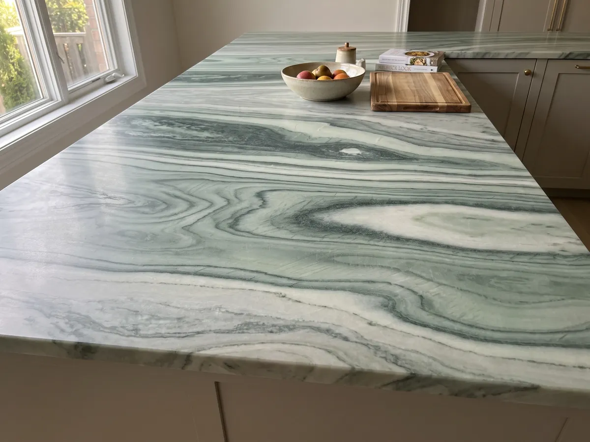 Kitchen island with a green Cipollino marble countertop and a straight edge in a naturally lit kitchen: wavy dark and light green bands forming an eye shape at the center