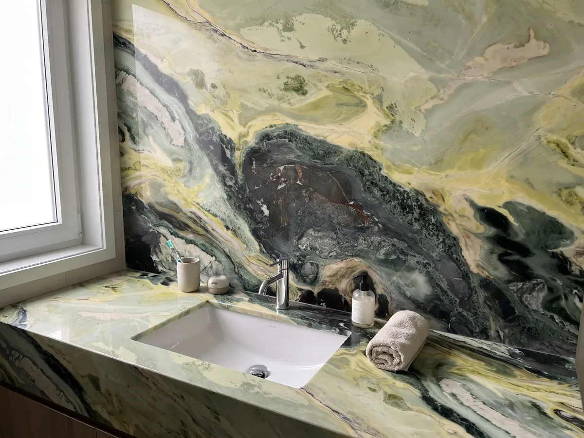 Bathroom vanity top and wall in green Dream Green marble with a white sink and chrome fixtures: dark green and lime yellow waves with a very dark central area
