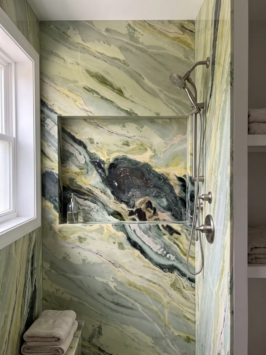 Shower clad in full slabs of green Dream Green marble with a recessed niche: dark green and lime yellow waves with a very dark central area