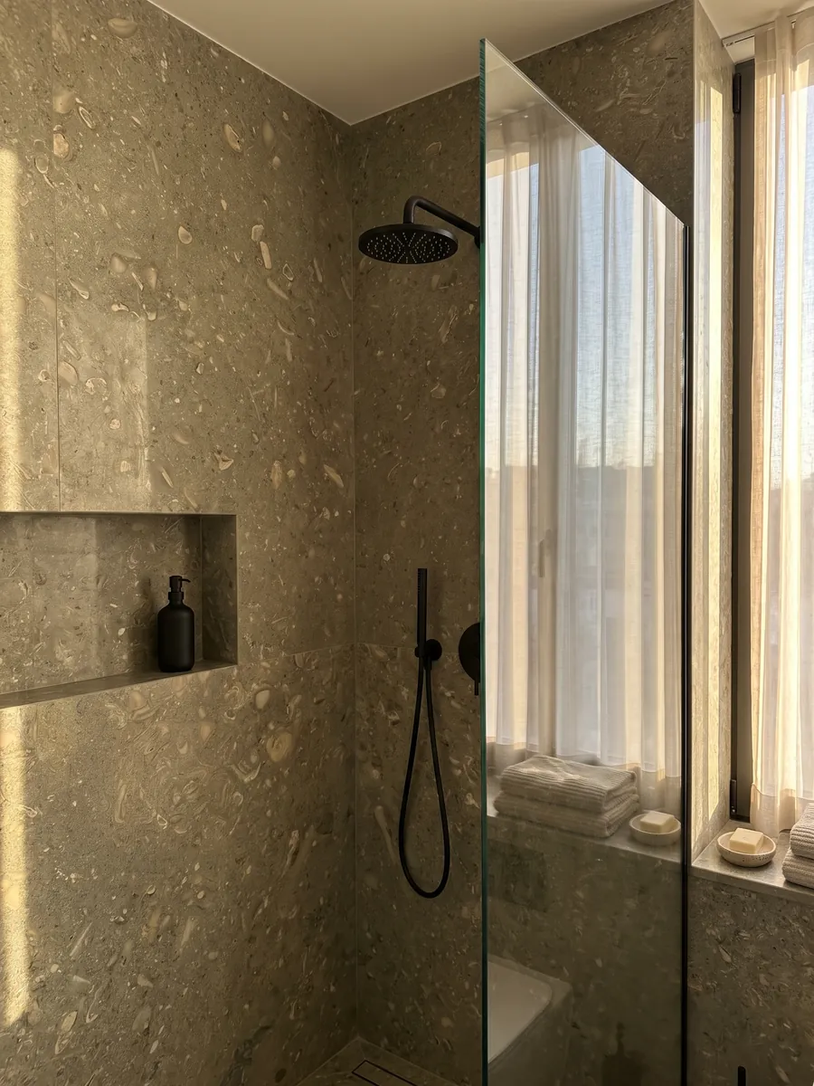 Shower clad in full slabs of green Fossil Green marble with a recessed niche: speckled olive green with fossil shell silhouettes in a lighter tone
