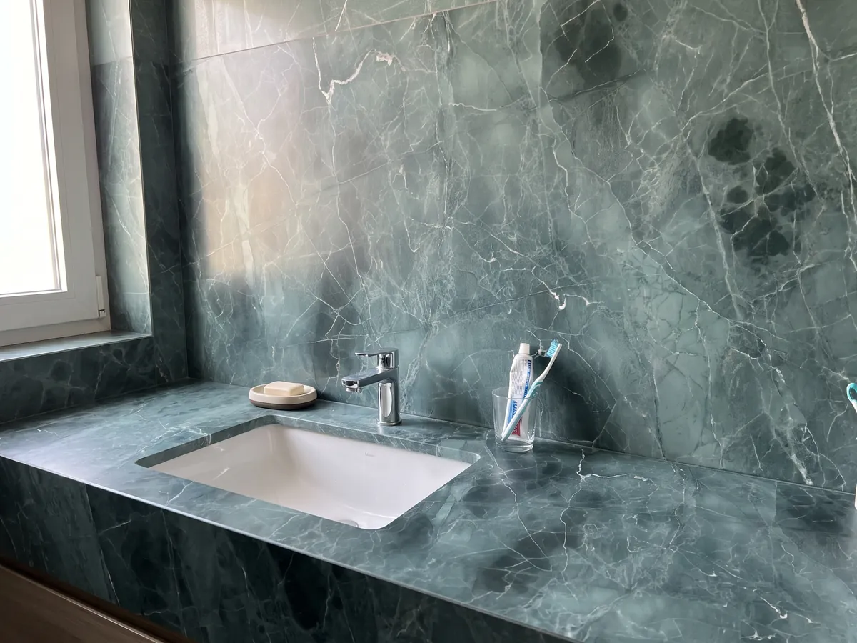 Vanity top and bathroom wall in Green Algae green marble with a white sink and chrome fixtures: teal with darker clouds and a network of fine white veins