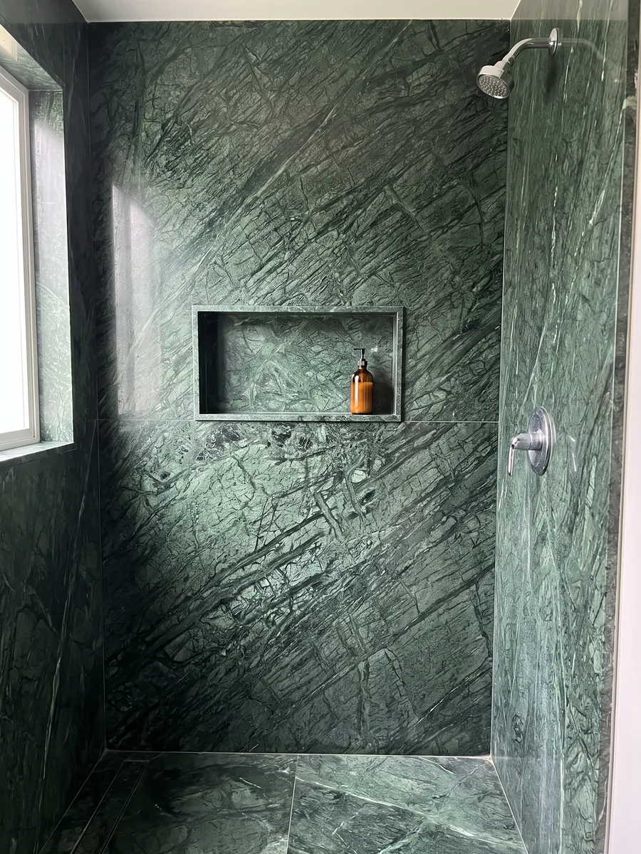 Shower clad in full Verde Guatemala marble slabs with a recessed niche: forest green with a mesh of lighter veins crossing diagonally