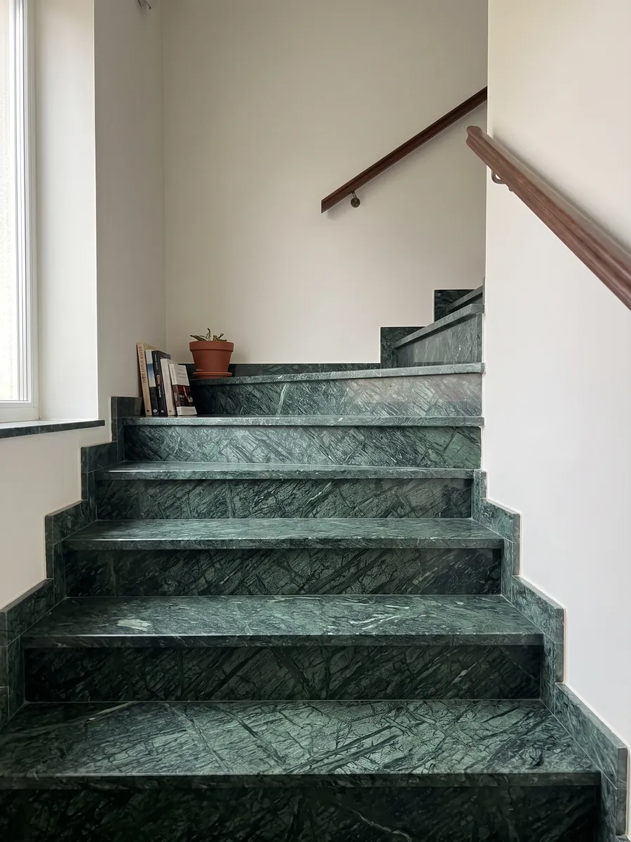 Indoor staircase with Verde Guatemala marble steps and a handrail: forest green with a mesh of lighter veins crossing diagonally
