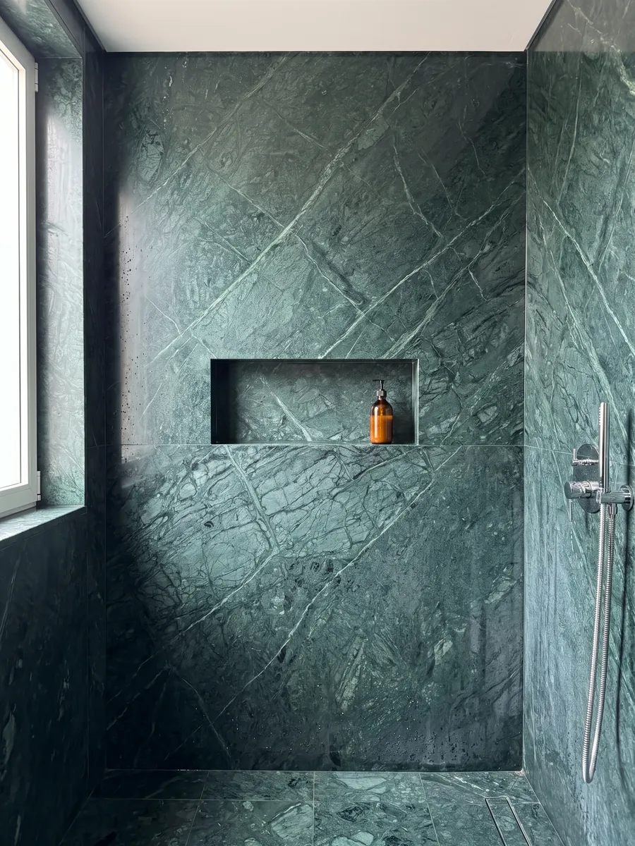 Shower clad in full Verde Imperiale marble slabs with a recessed niche: deep petrol green with fine lighter veins crossing on the diagonal