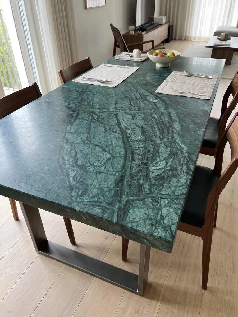 Dining table with a Verde Imperiale marble top on a steel base: deep petrol green with fine lighter veins crossing on the diagonal