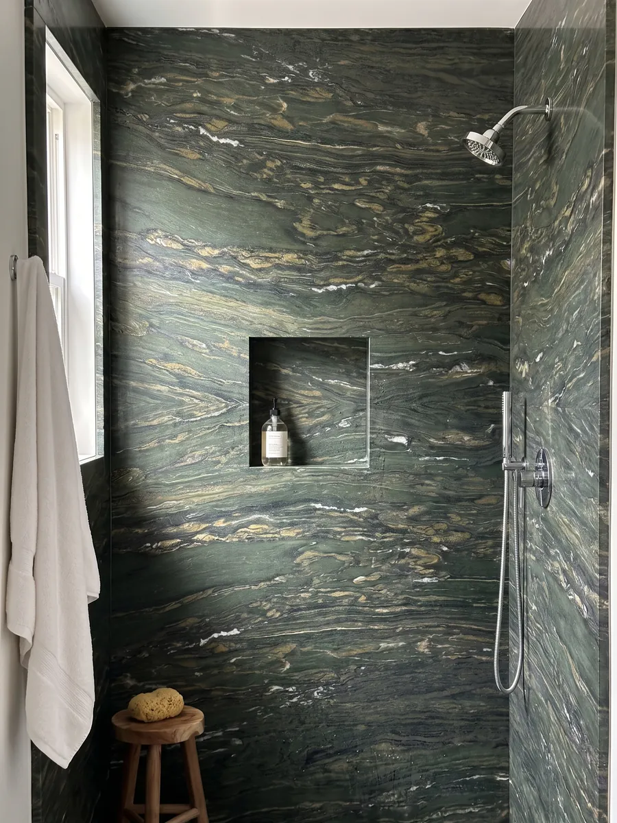 Shower clad in full Verde Pavone marble slabs with a recessed niche: deep green with golden and white strokes flowing horizontally