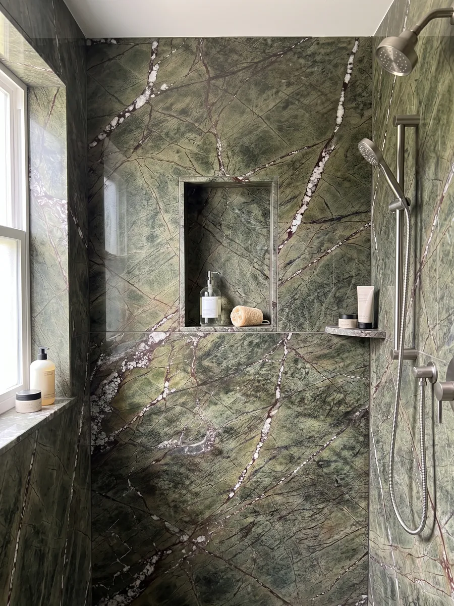 Shower lined with full slabs of green Picasso Green marble with a recessed niche: olive green with a network of reddish veins and white diagonal veins