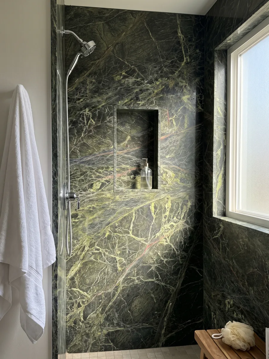 Shower lined with full slabs of Rainforest Green marble and a recessed niche: dark green covered by a dense web of yellow-green veins