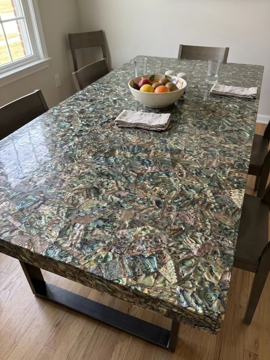 Dining table with an abalone mother of pearl top on a steel base: a tight mosaic of iridescent shell in greens, blues and browns